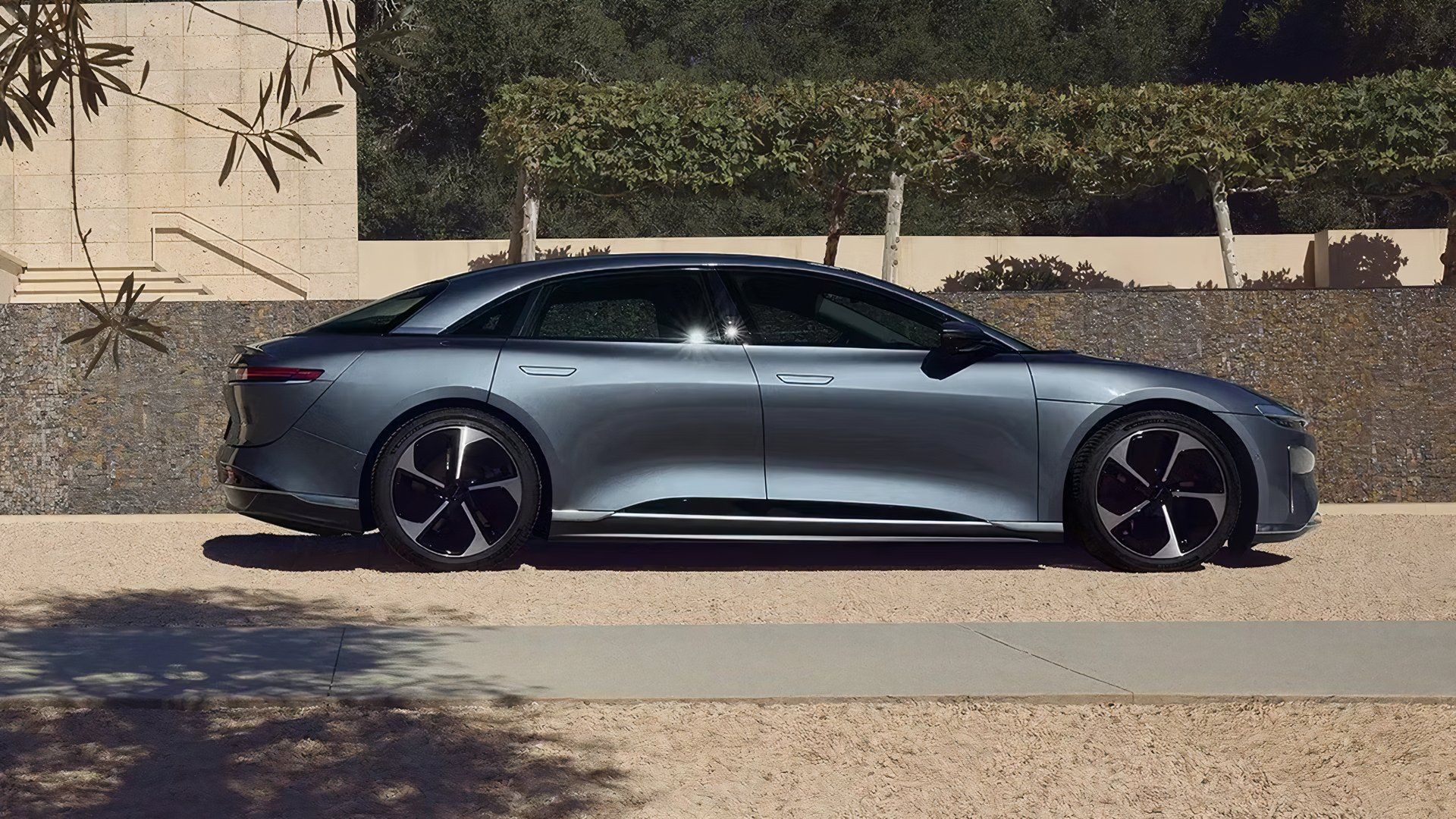 A static profile shot of a silver Lucid Air Pure parked by a modern house
