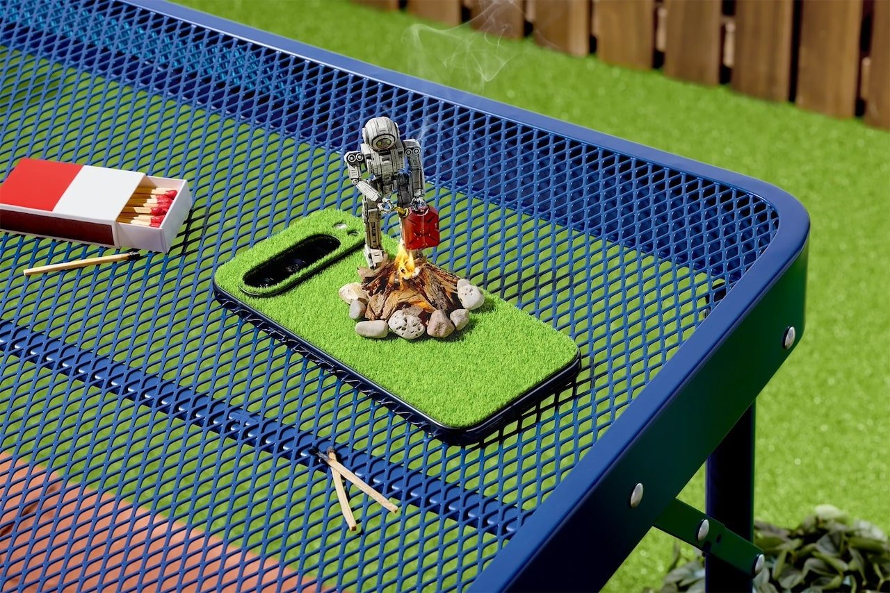 Tiny robot lighting camp fire on Google Pixel phone covered in synthetic grass
