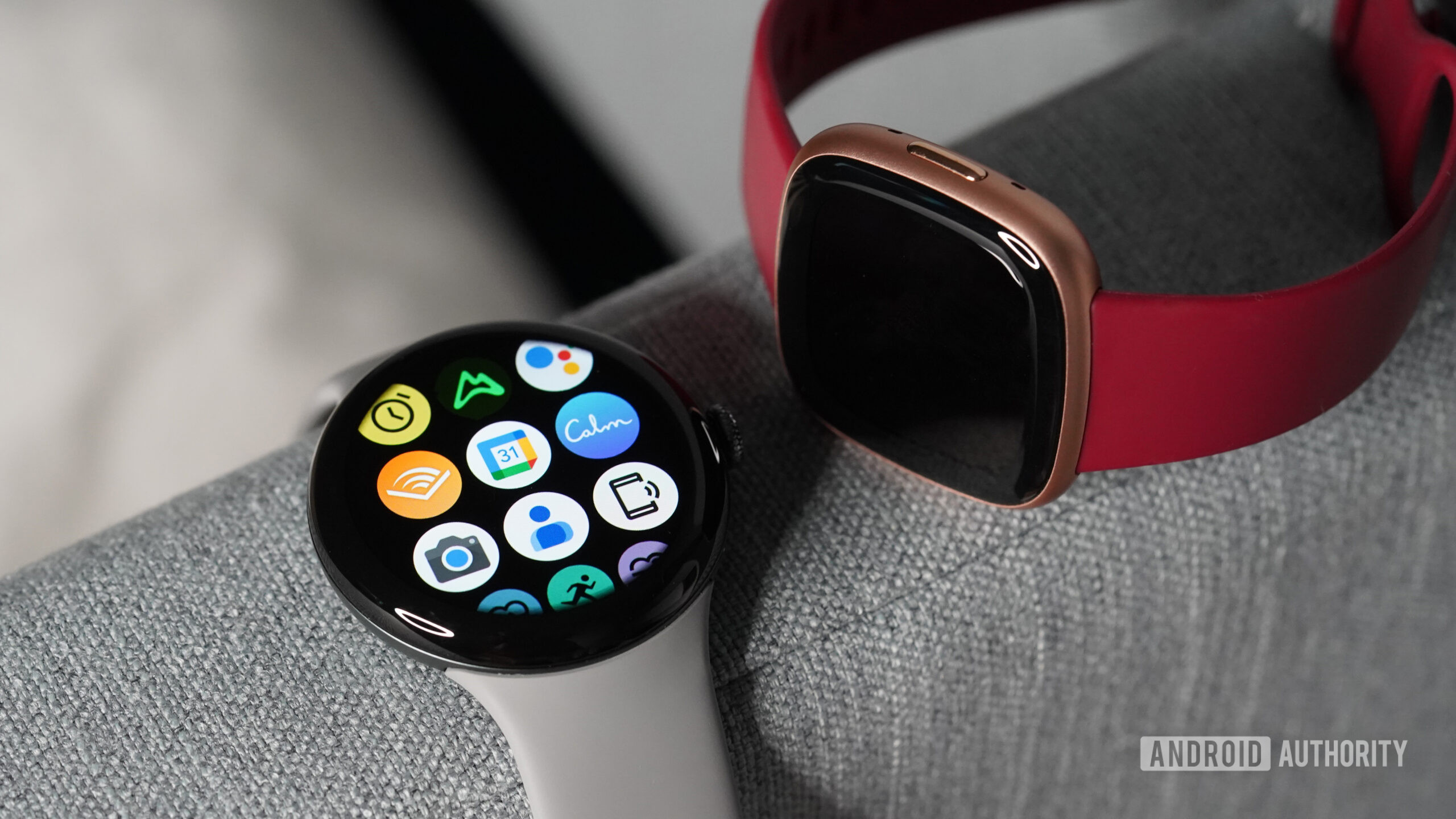 Pixel Watch Fitbit Apps A Pixel Watch displays its app library next to a Fitbit Versa 4.