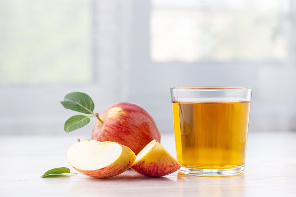 Glass of apple juice and ripe red apples with leaves on a table.