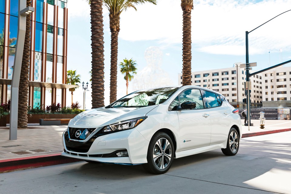 White Nissan Leaf electric hatchback parked on city street.