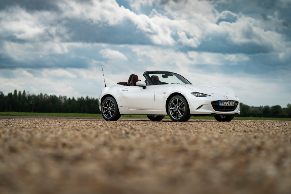 White Mazda MX-5 convertible parked on gravel.