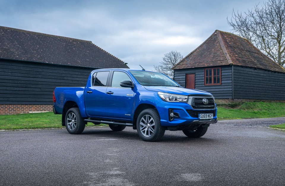 Blue Toyota Hilux parked in front of barns.