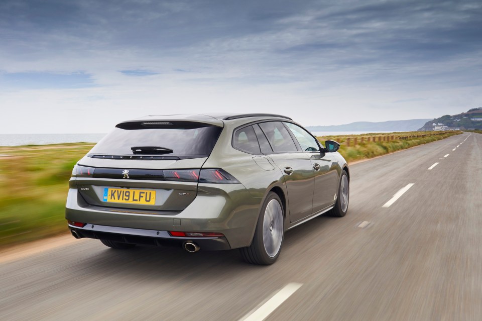 A green Peugeot 508 SW GT driving on a coastal road.