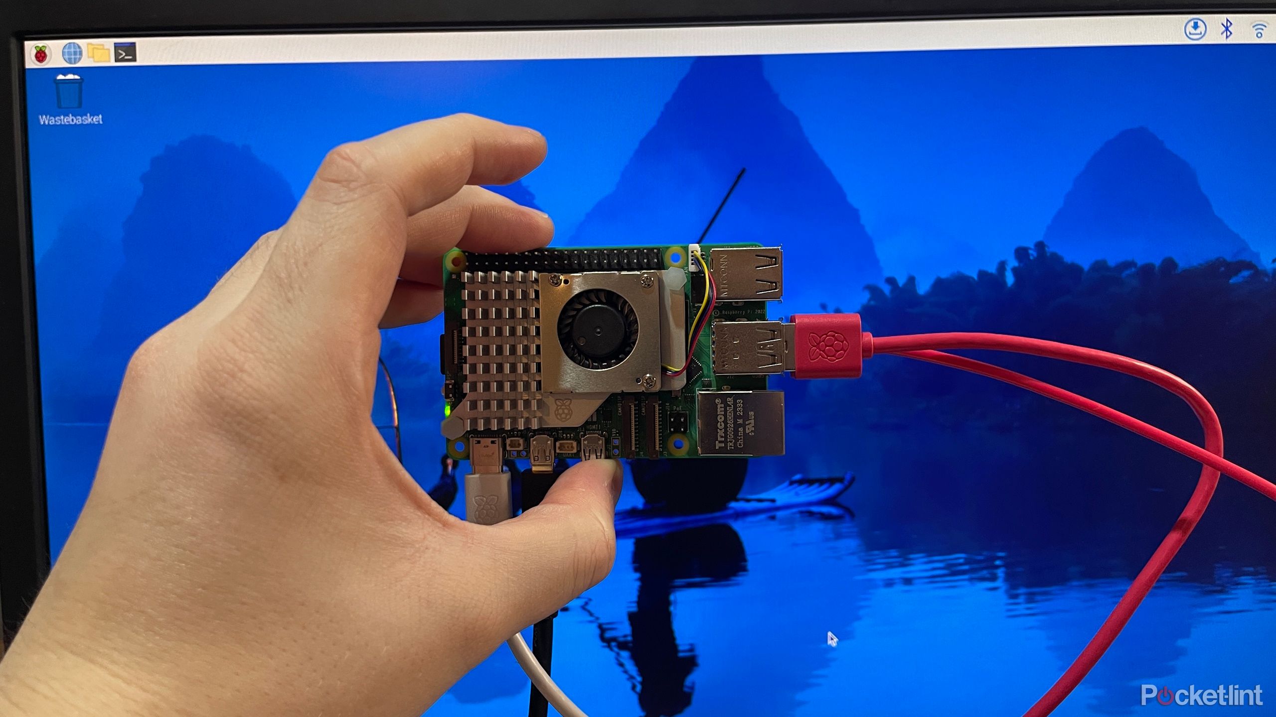 Raspberry Pi 5 being held in front of a screen with Raspberry Pi OS on