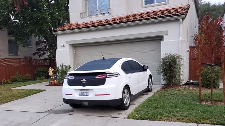 An electric vehicle (EV) is parked in front of a greige garage door