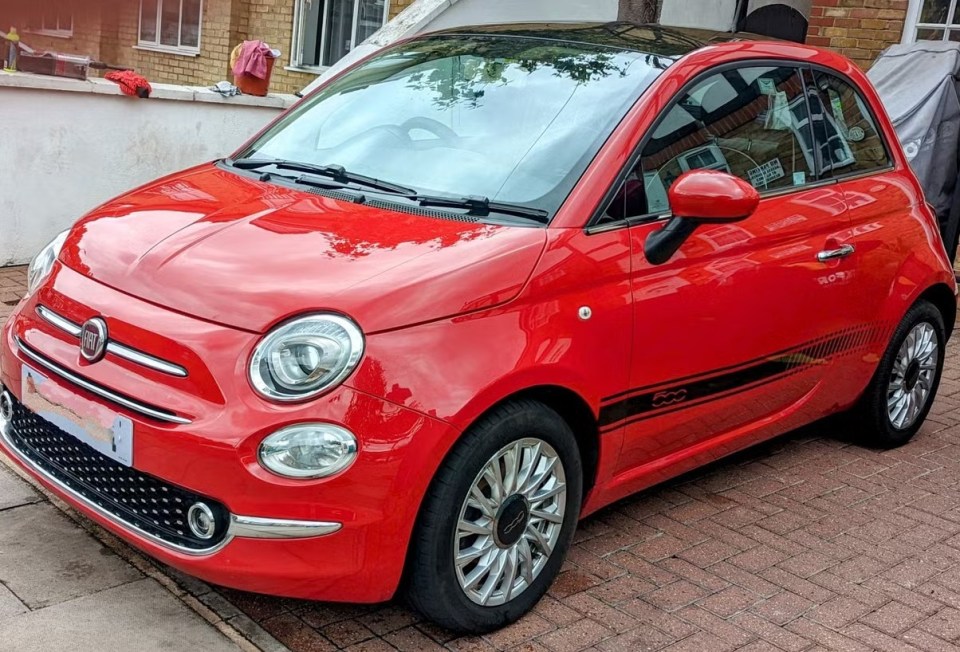 Red Fiat 500 parked on a brick driveway.