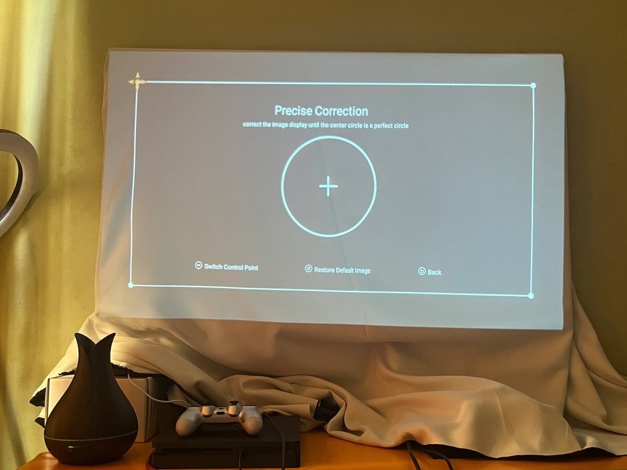 Projected image correction setup on white cloth draped over table with game controller and air diffuser beneath