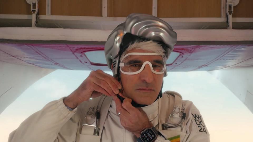 Apple's Craig Federighi, standing at a plane's rear camp, strapping on a hair-shaped helmet.