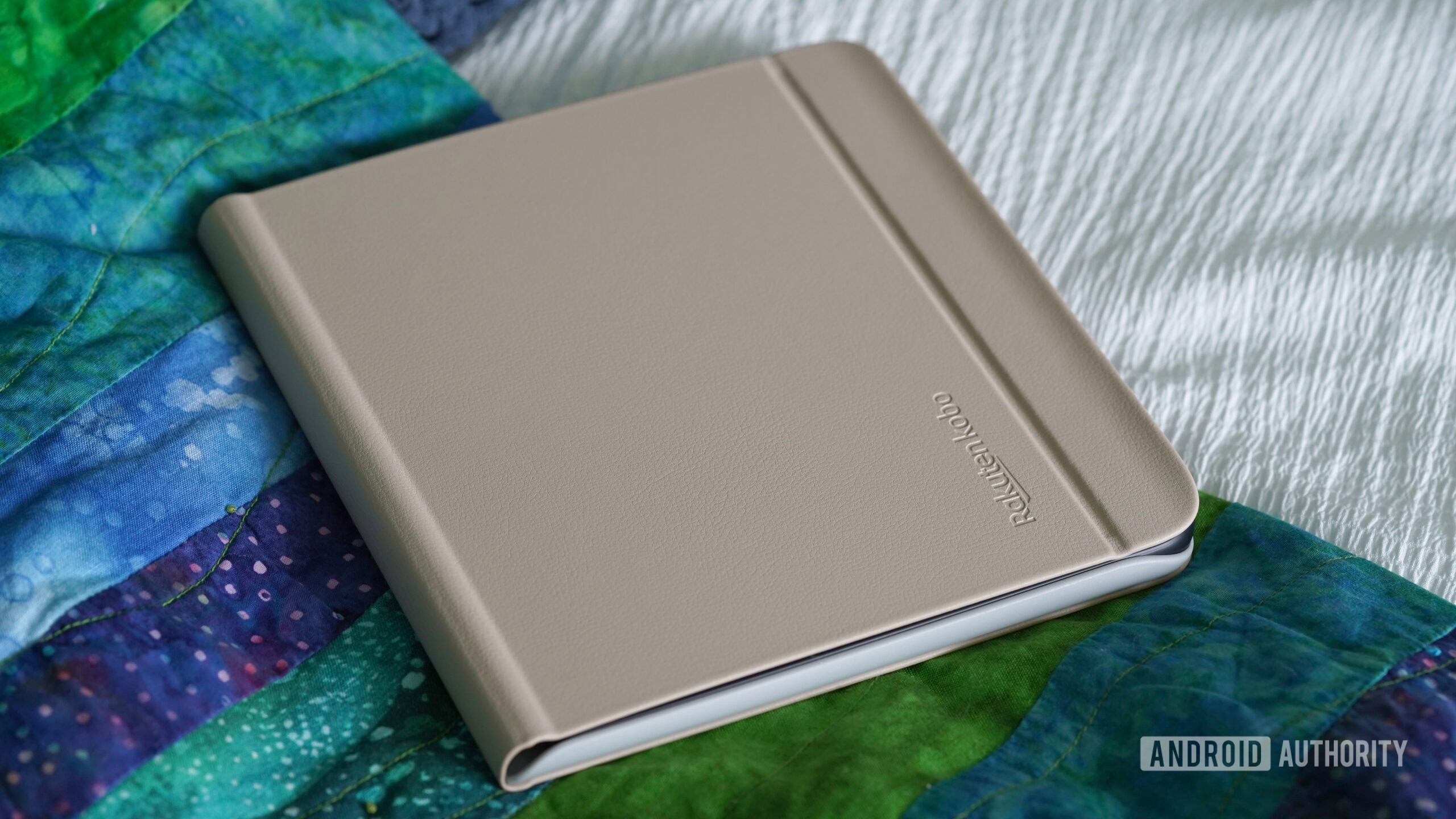 Kobo Libra Colour Sleepcover A Kobo Libra Colour in a beige SleepCover rests on a bed.
