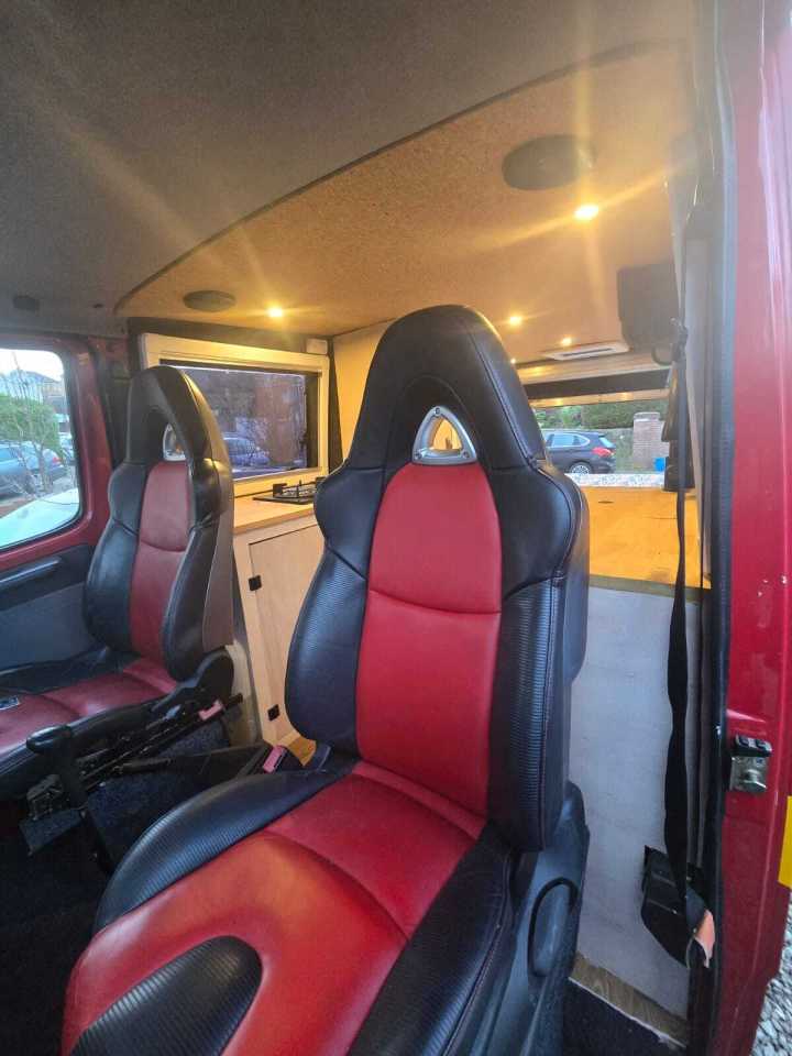 Interior of a campervan conversion of a retired fire engine, showing red and black bucket seats.