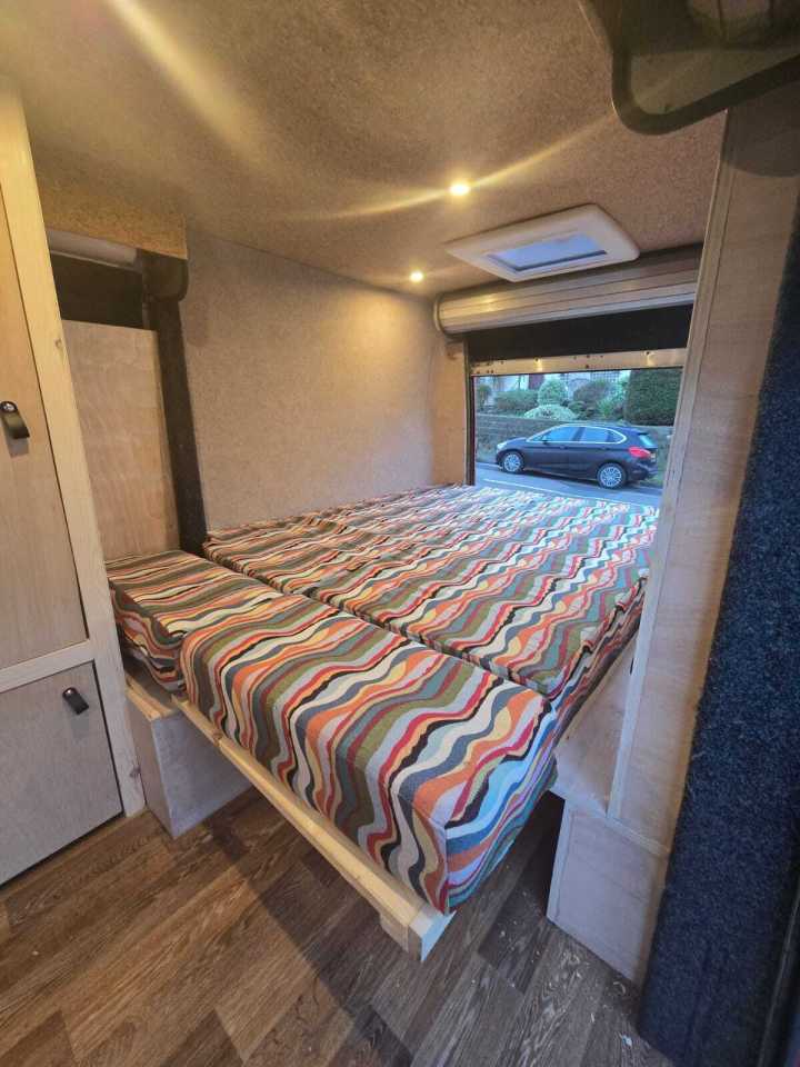 Interior of campervan conversion showing a bed with multicolored striped bedding.