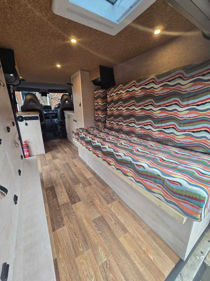 Interior of a campervan conversion, showing a sofa bed and wood flooring.