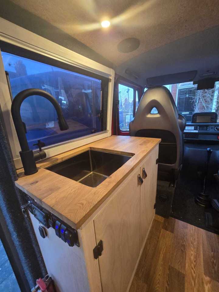 Interior of a campervan conversion, showing a wooden countertop with a sink and faucet.