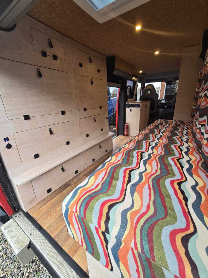 Interior of a campervan conversion, showing built-in cabinets and a bed with colorful upholstery.