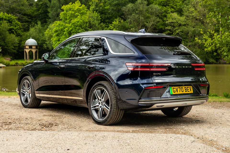 Rear view of a dark blue Genesis GV70 parked by a lake.