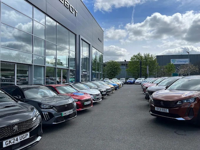 Row of Peugeot cars parked outside a dealership.