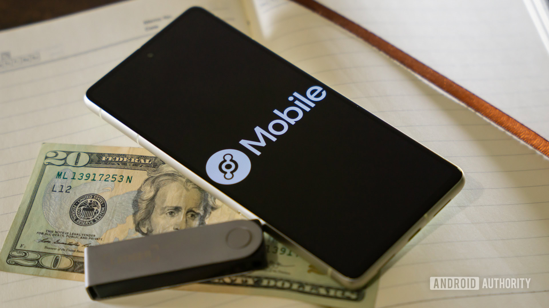Helium Mobile logo on smartphone, next to money and crypto hardware wallet (2) Helium Mobile logo on smartphone, next to money and crypto hardware wallet (2)