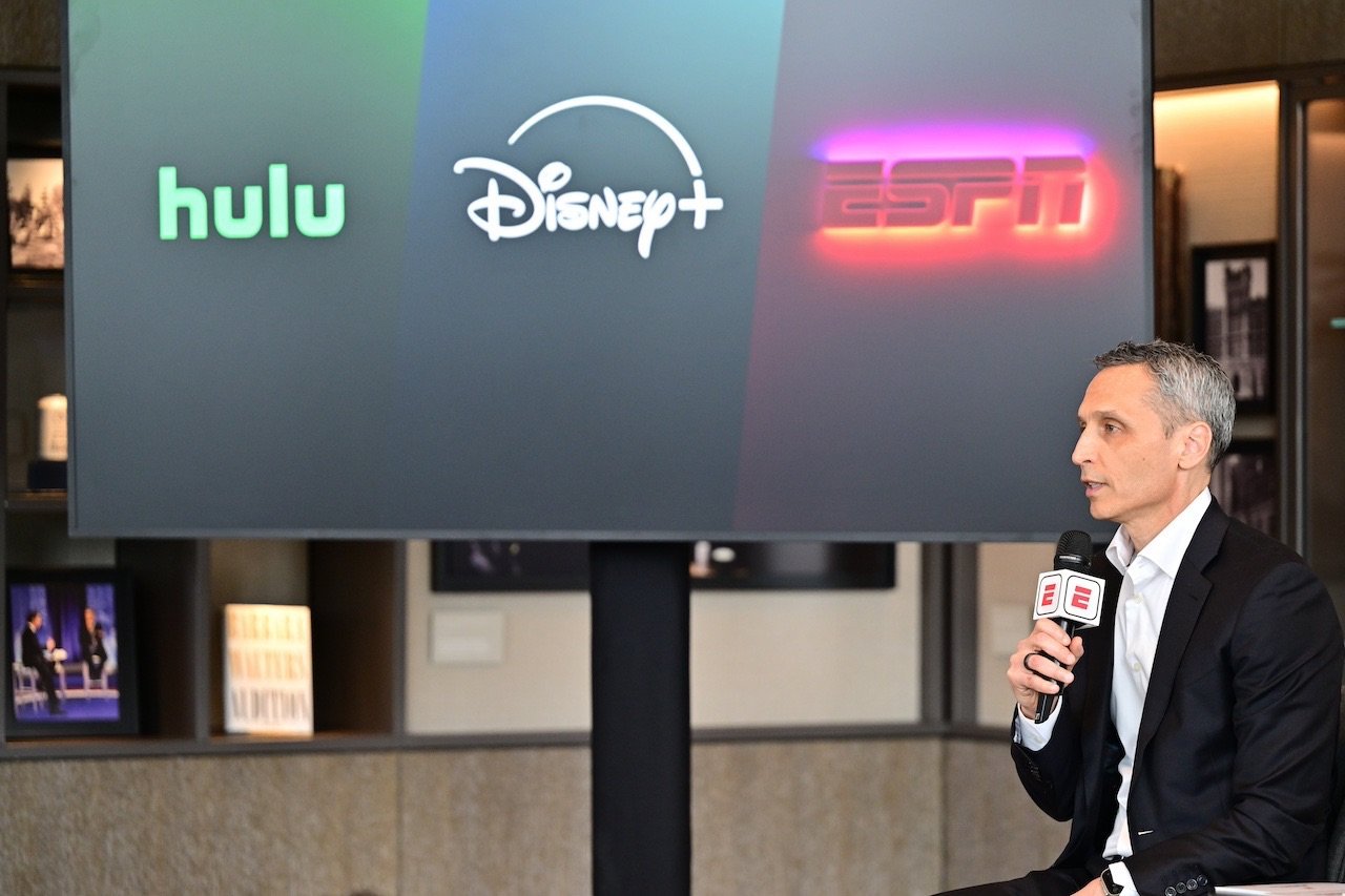 ESPN Chairman speaking with microphone in front of TV showing different streaming channels