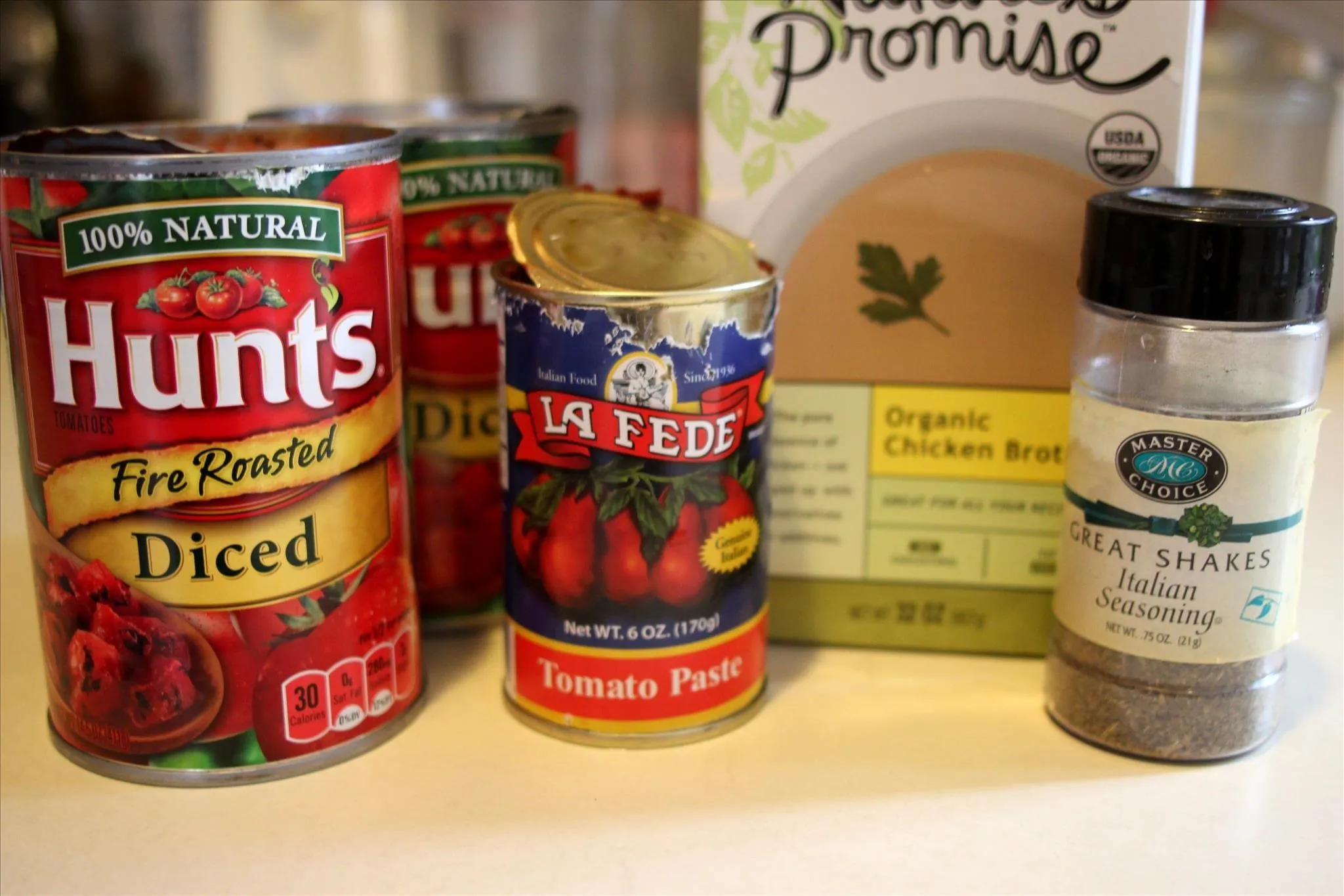 Canned tomatoes, tomato paste, organic chicken broth, and seasoning jar.