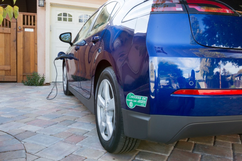 Blue plug-in electric car charging in a driveway.