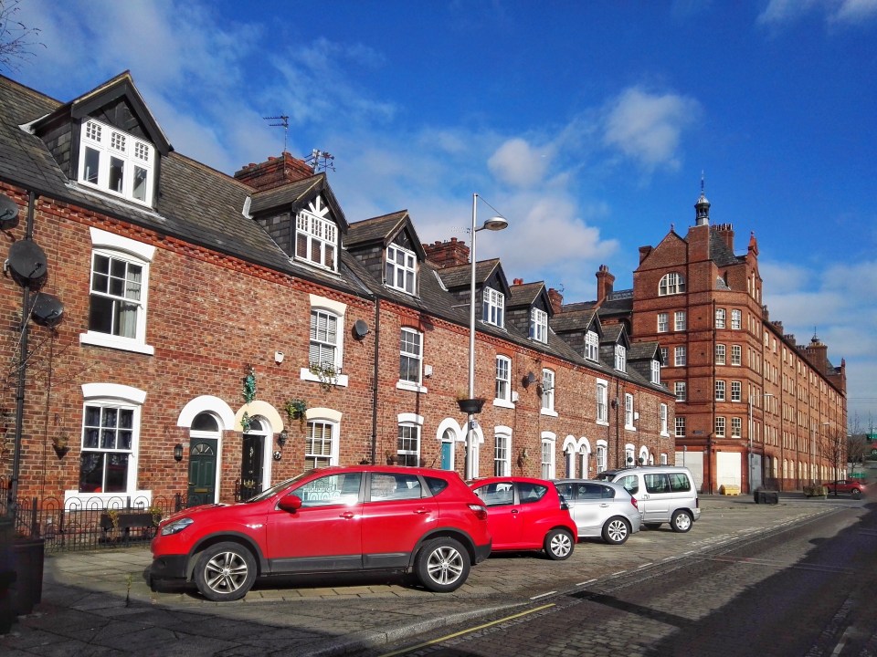 Row of brick houses in Manchester, England, with parked cars.