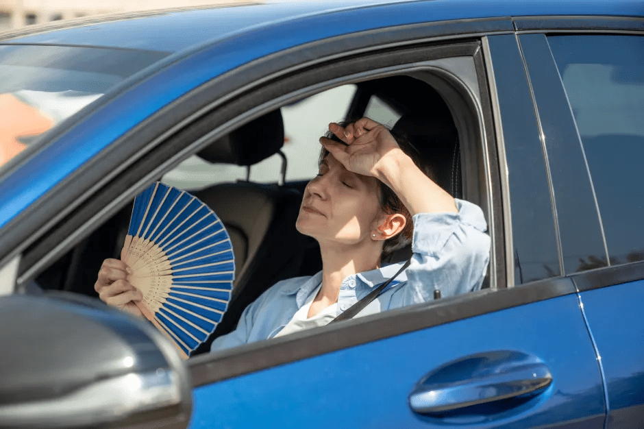 Woman in a hot car using a hand fan.