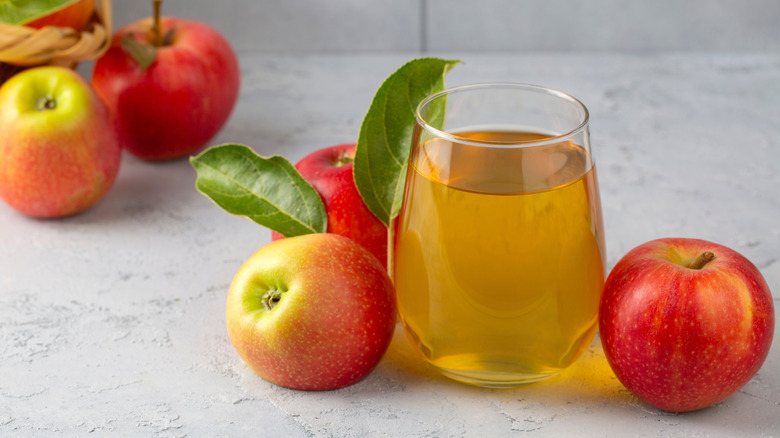 glass of apple juice on a counter surrounded by freshly picked apples