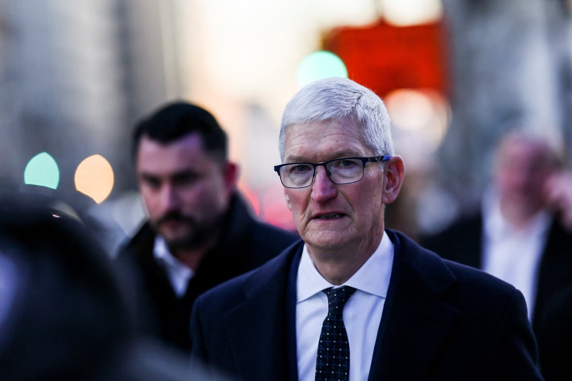 A man with white hair and glasses stands on a street.