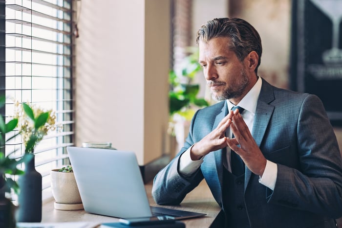 A well-dressed investor looks at computer with a contemplative expression.