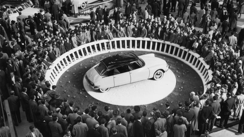 White Citroën DS on an auto show stage surrounded by people