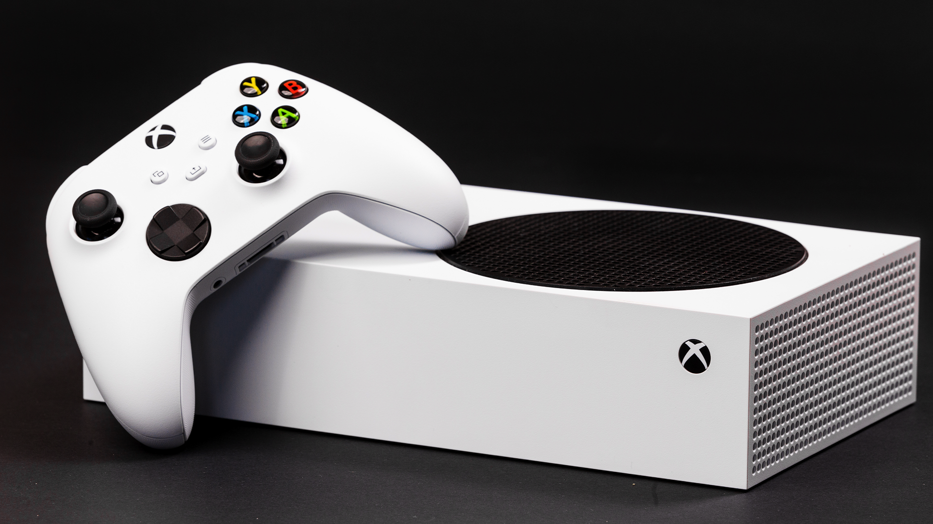 An Xbox Series S placed horizontally with an Xbox Series controller resting on it. 