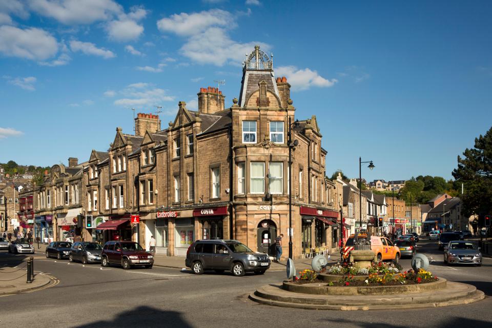 Crown Square in Matlock, Derbyshire, England.  Shops and buildings line the street, with a traffic circle in the foreground.