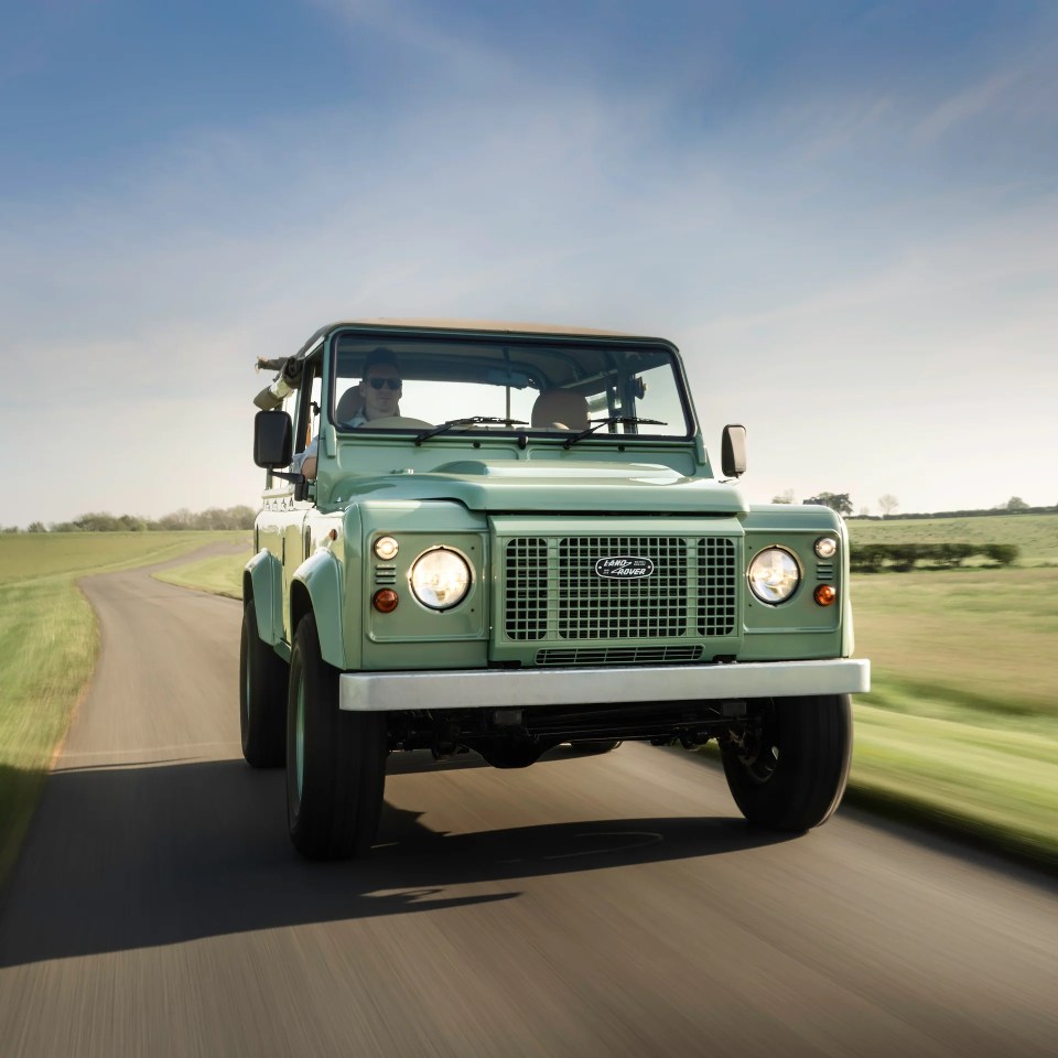 Light green Land Rover Defender driving down a country road.