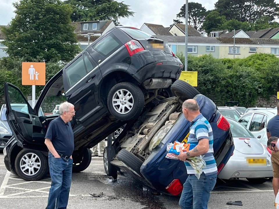 A black SUV on top of a blue car in a parking lot.