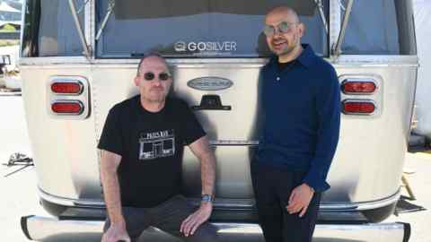 Two men stand behind a silver vehicle